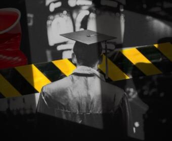 Graduate in cap and gown seen from behind with yellow-and-black caution tape across the foreground.