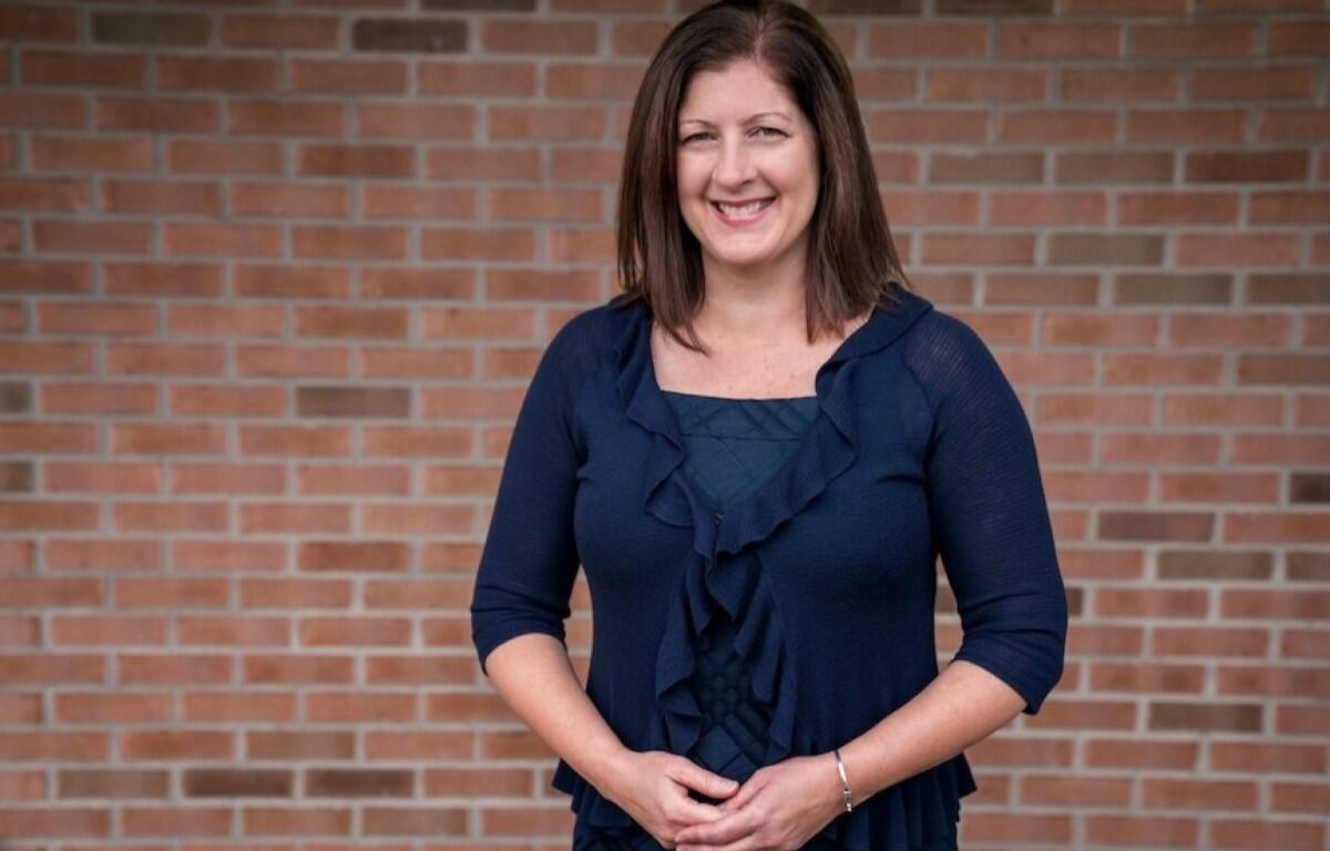 Smiling woman in a navy ruffled cardigan standing against a brick wall.