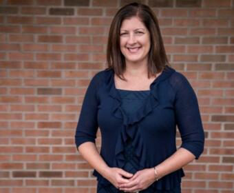 Smiling woman in a navy ruffled cardigan standing against a brick wall.
