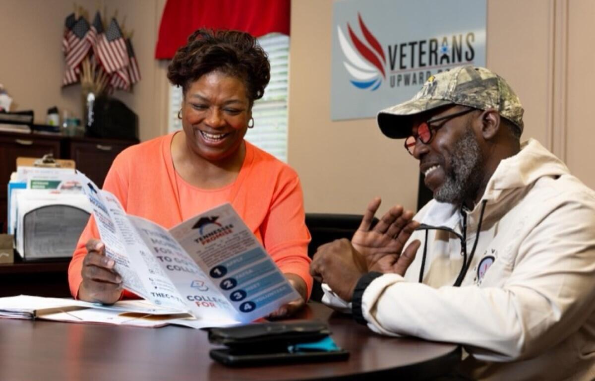 Two adults sit at a desk reading a brochure; a Veterans Upward Bound sign is on the wall behind them.