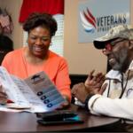 Two adults sit at a desk reading a brochure; a Veterans Upward Bound sign is on the wall behind them.