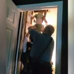 Two police officers lift a child up through an open doorway into a brightly lit room in a stairwell area.