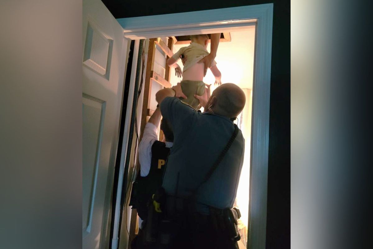 Two police officers lift a child up through an open doorway into a brightly lit room in a stairwell area.