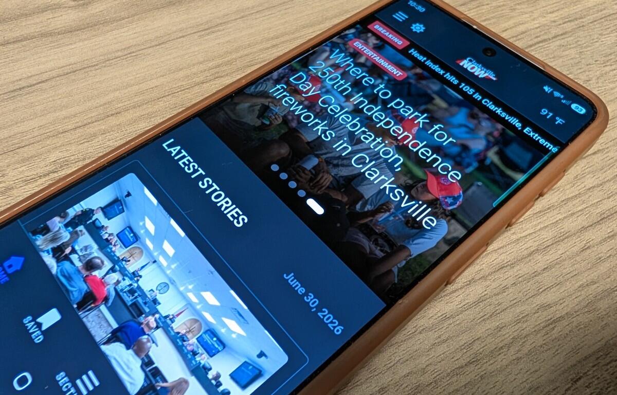 Smartphone on a wooden surface showing a news app with 'LATEST STORIES' and event photos.