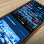 Smartphone on a wooden surface showing a news app with 'LATEST STORIES' and event photos.