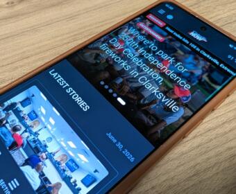Smartphone on a wooden surface showing a news app with 'LATEST STORIES' and event photos.