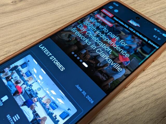 Smartphone on a wooden surface showing a news app with 'LATEST STORIES' and event photos.