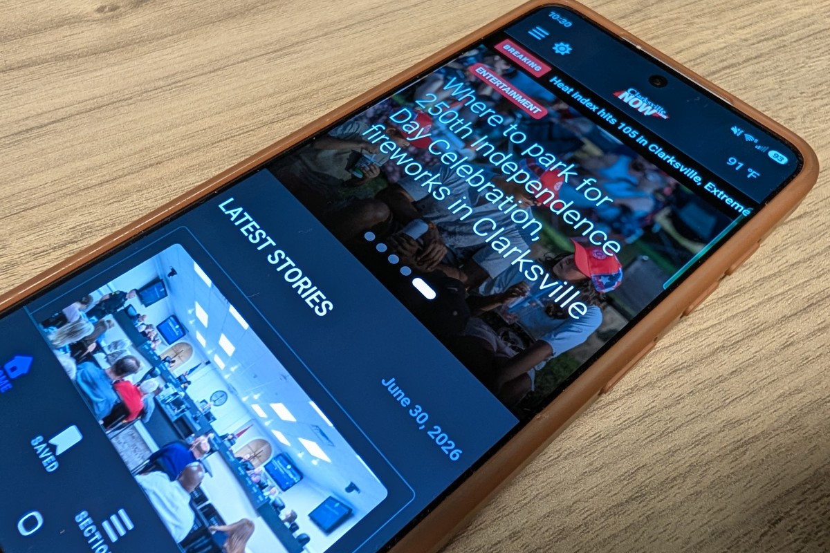 Smartphone on a wooden surface showing a news app with 'LATEST STORIES' and event photos.