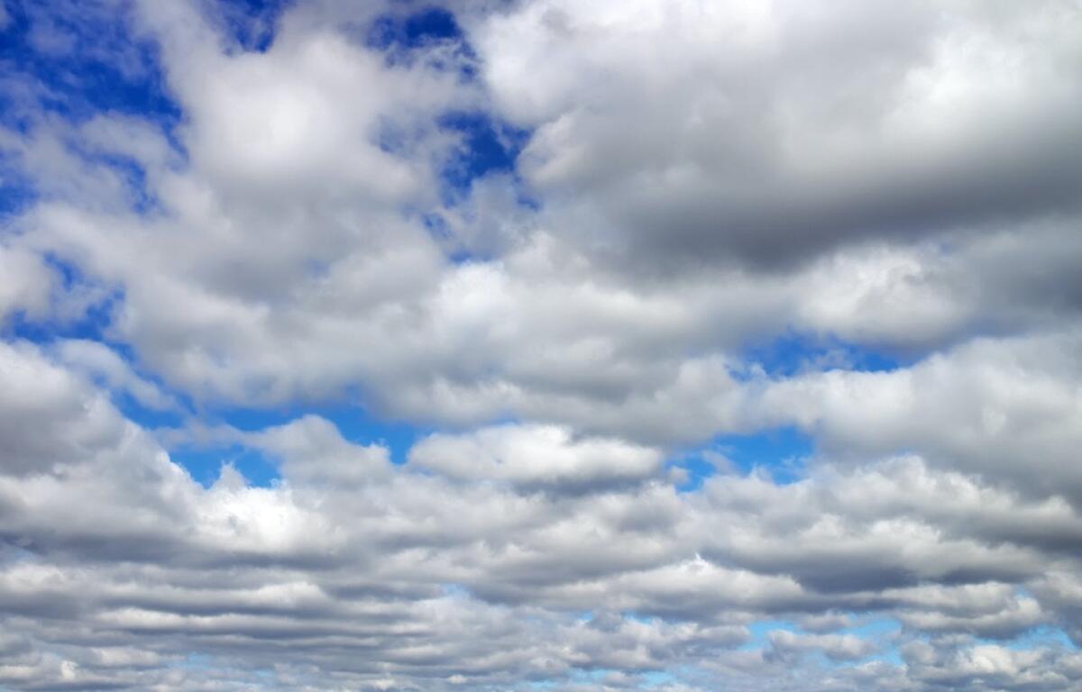 Wide sky filled with low, fluffy white clouds and blue gaps visible between cloud layers