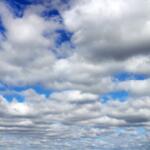 Wide sky filled with low, fluffy white clouds and blue gaps visible between cloud layers