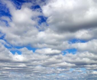 Wide sky filled with low, fluffy white clouds and blue gaps visible between cloud layers