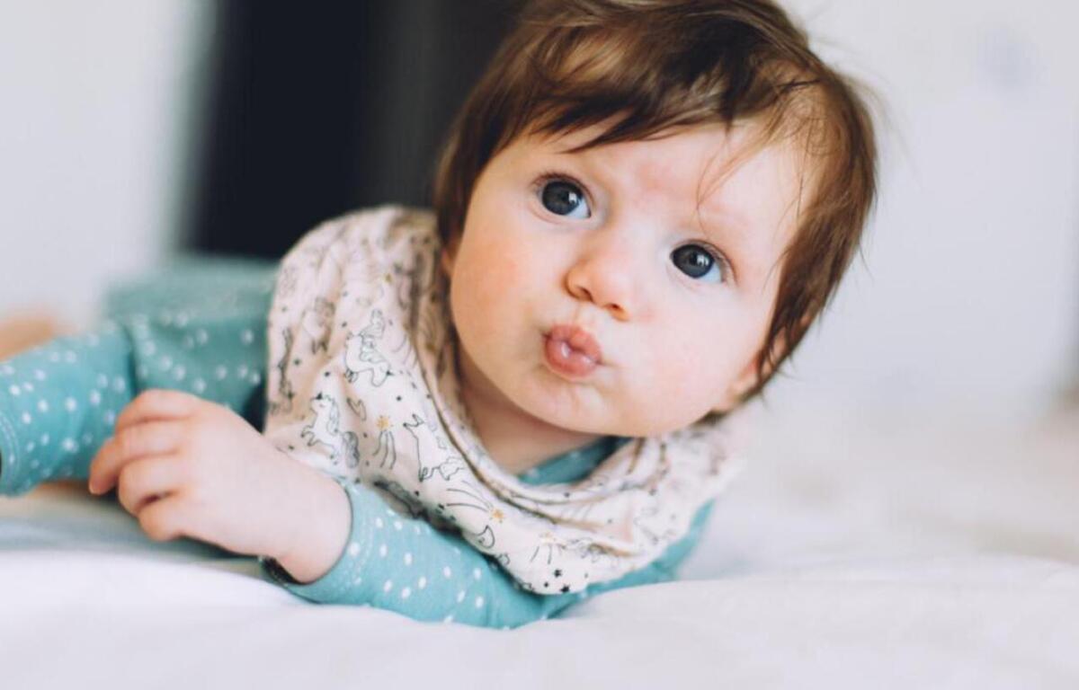 Baby lying on a bed, looking at the camera and puckering lips.
