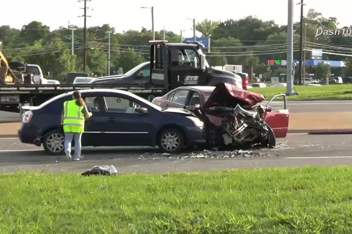 Two-car crash on a highway: a blue sedan rear‑ended by a red car with extensive front damage; a worker in a neon vest stands nearby on the road.