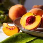 Halved ripe peach on a metal plate, bright orange flesh around a red seed, with whole peaches in the background.