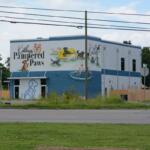 Two-story blue-gray building with a colorful dog mural that reads 'Kathy's Pampered Paws' and shows dogs at play and a fountain scene.