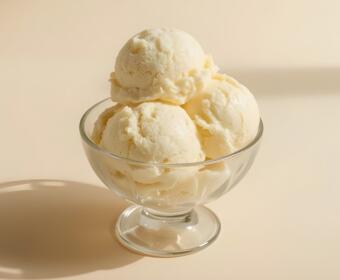 Vanilla ice cream scoops stacked in a clear glass dessert bowl on a pale background, with a soft shadow nearby.