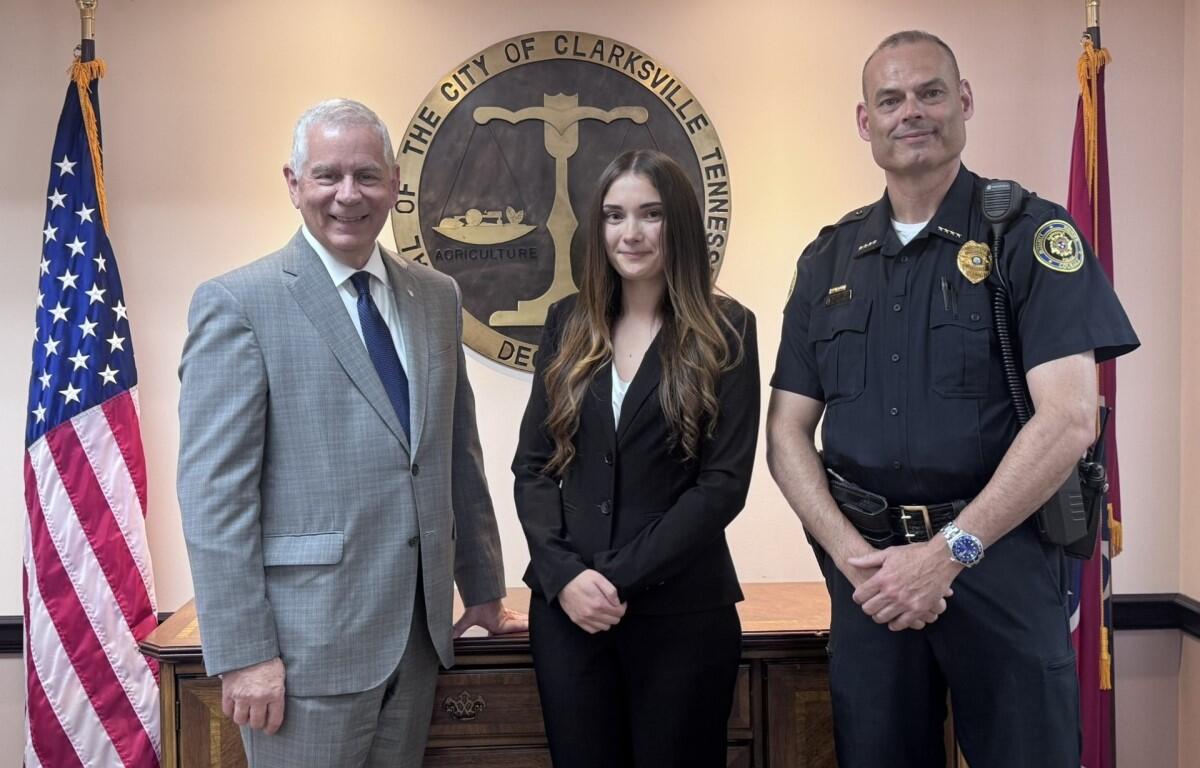 Three people pose in front of the Clarksville, TN city seal: a man in a gray suit, a woman in a black blazer, and a uniformed officer.