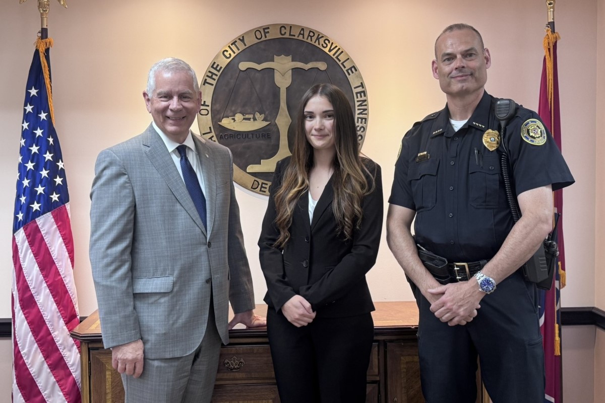 Three people pose in front of the Clarksville, TN city seal: a man in a gray suit, a woman in a black blazer, and a uniformed officer.