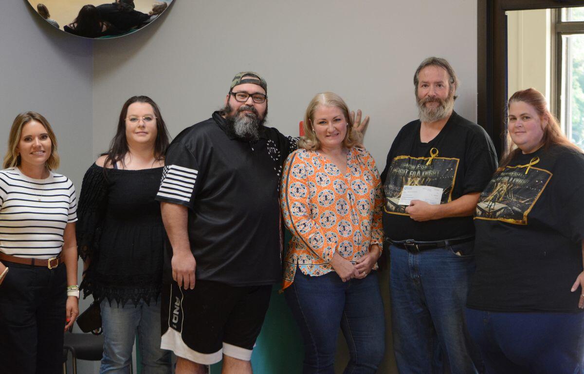 Six adults standing in a line indoors, smiling for a group photo in a community room or office space.