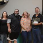 Six adults standing in a line indoors, smiling for a group photo in a community room or office space.