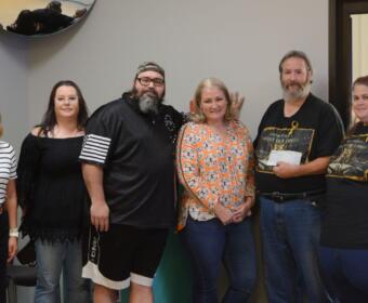 Six adults standing in a line indoors, smiling for a group photo in a community room or office space.