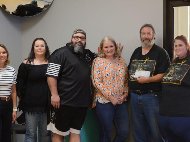 Six adults standing in a line indoors, smiling for a group photo in a community room or office space.