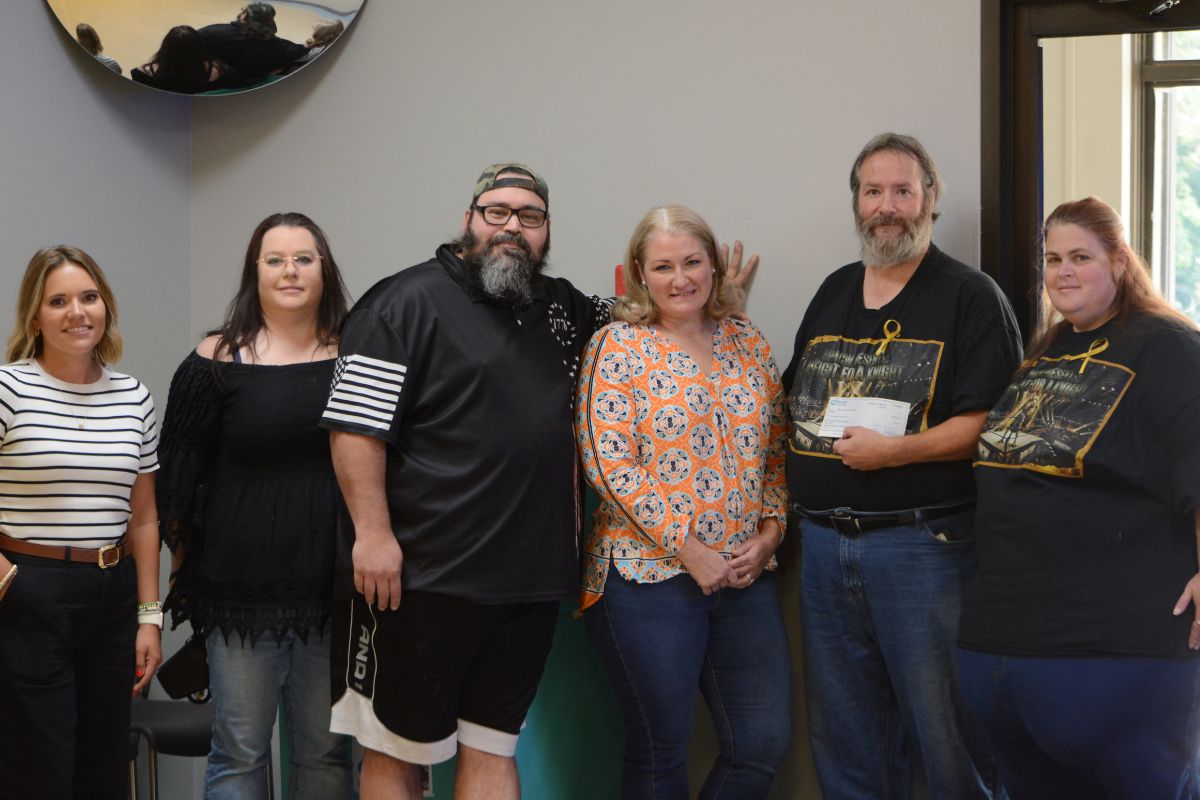 Six adults standing in a line indoors, smiling for a group photo in a community room or office space.