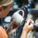 Potter shaping a gray ceramic mug with a sculpting tool in a pottery studio