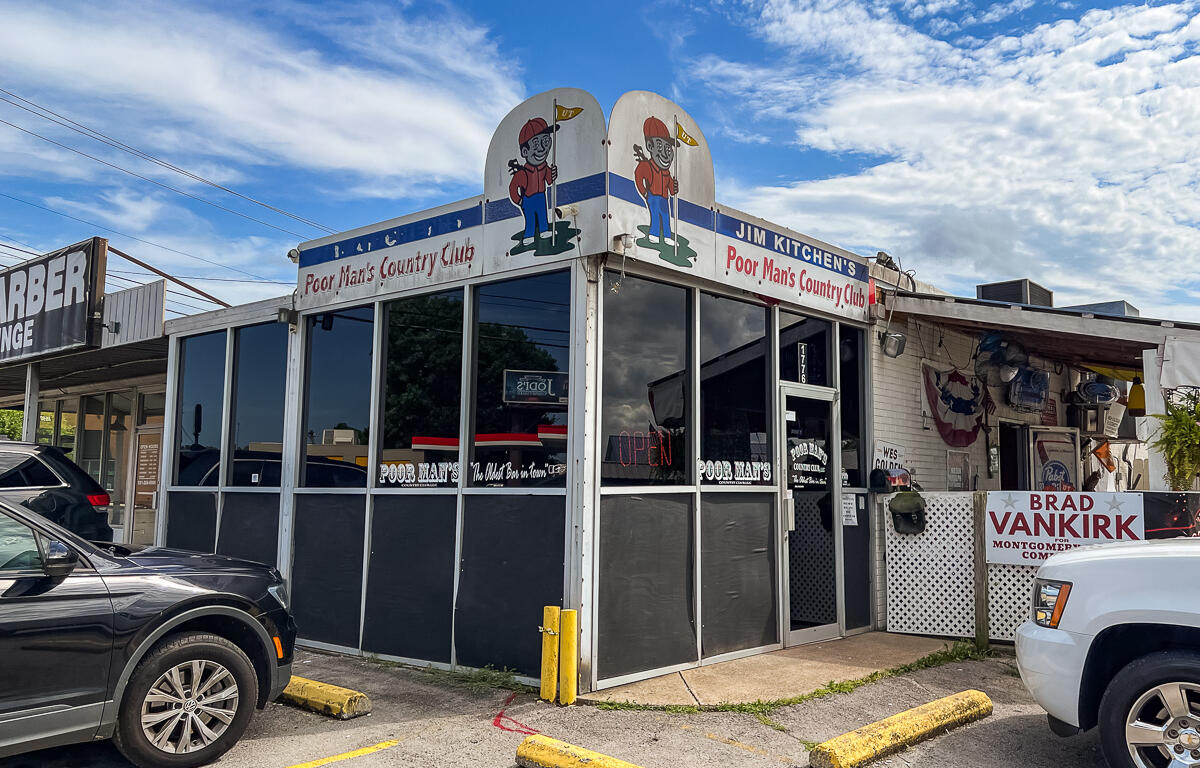 Exterior of Jim Kitchen's Poor Man's Country Club, a small diner with cartoon mascots on the roof and large glass windows in front.