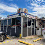 Exterior of Jim Kitchen's Poor Man's Country Club, a small diner with cartoon mascots on the roof and large glass windows in front.