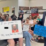 Attendees holding signs up toward the board at the CMCSS formal school board meeting on July 21, 2026. (Jazmin Logan)