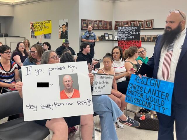 Attendees holding signs up toward the board at the CMCSS formal school board meeting on July 21, 2026. (Jazmin Logan)