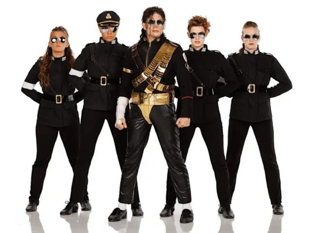 Five people stand in a line wearing black military-style outfits with belts and sunglasses; center performer wears gold accessories and sash.